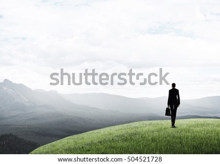 Elegant businesswoman standing on green hill and looking ahead