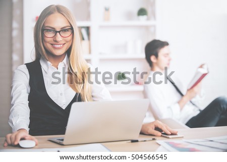 Portrait of beautiful european woman at modern workplace with laptop and reading colleague in the background
