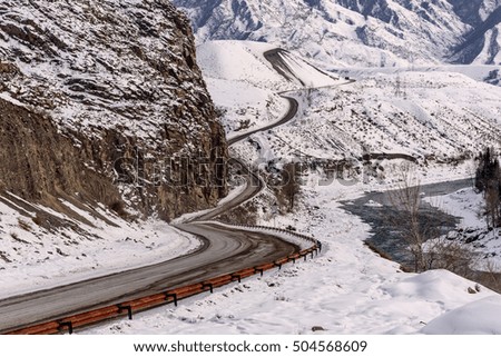 Scenic winter view with the winding asphalt road, river and trees on a background of mountains covered with snow