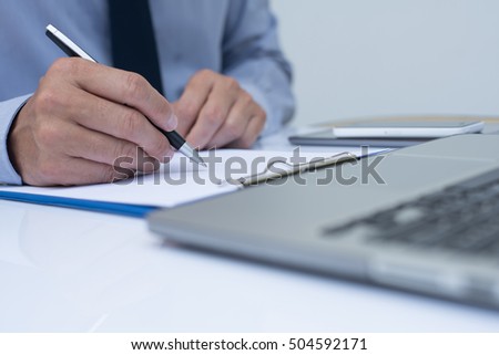 Business man writing on notepad and working on laptop computer in office room, close up.