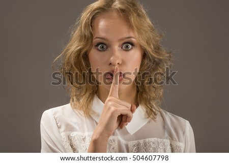 Portrait of expressive business woman with finger on lips, gesturing for quiet, studio shot on gray background. Showing the silence sign