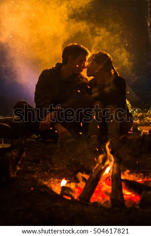 man kissing woman about the fire on the background of the starry sky.