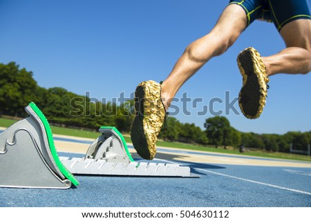 Athlete in gold shoes starting a race from the starting blocks on a blue running track 