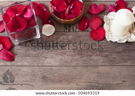Glass vase and wood bow filled with red and white rose petals, white aromatic vanilla candle. Wooden background. Aromatherapy concept. Romantic background. Rose frame with copy space