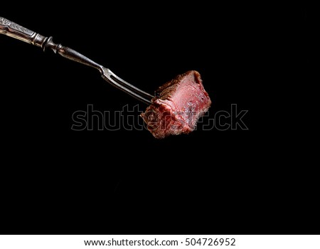 Slices of Medium rare grilled Steak Ribeye on meat fork on  black background Royalty-Free Stock Photo #504726952