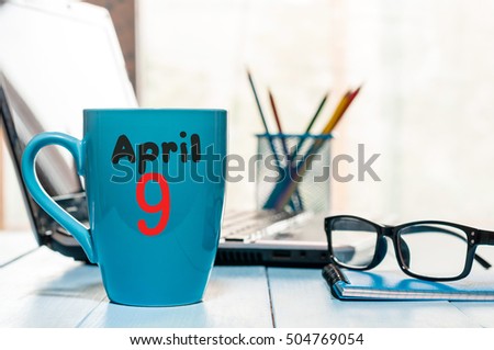 April 9th. Day 9 of month, calendar on morning coffee cup, business office background, workplace with laptop and glasses. Spring time, empty space for text