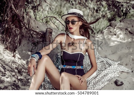 Beautiful bohemian styled and tanned girl at the beach in sunlight wearing swimsuit and hat