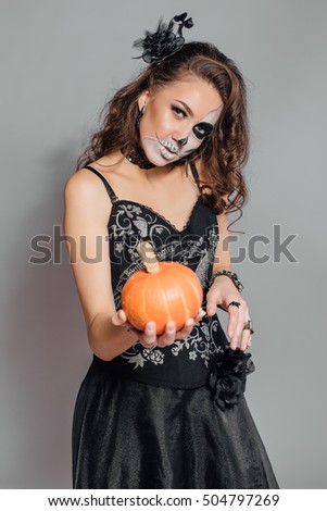 Young woman in black with half face skull make-up and pumpkin in hand.