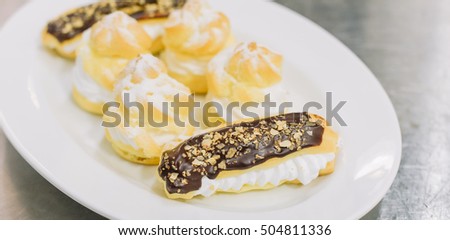 Assorted cream puffs filled with pastry cream and sprinkled with powdered sugar and dip in dark chocolate on a plate.selective focus on dipped chocolate puff pastry.toned image