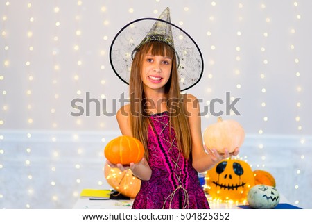 Teenager girl in witch costume posing with pumpkins and bottle of blue potion during Halloween party