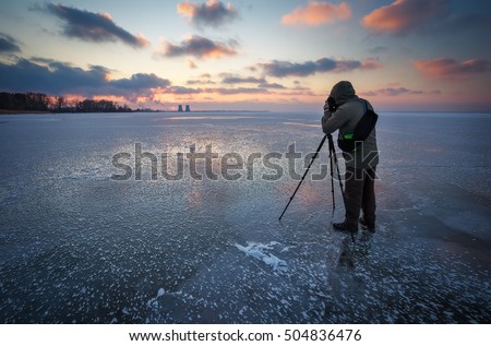 Photographer takes a picture of sunset on a frozen river in winter


