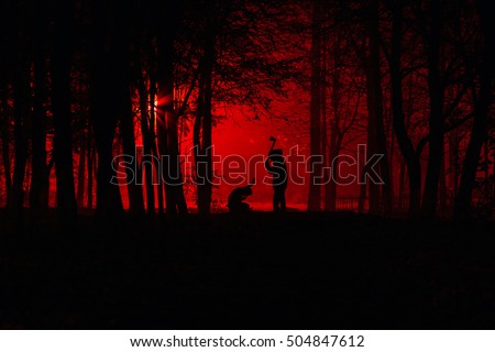 Maniac swings ax on his prey. Murder in the park. Maniac kills his victim in the night deserted park. Silhouettes in night foggy forest Royalty-Free Stock Photo #504847612