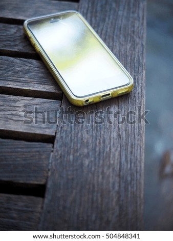 old green broken smartphone in transparent silicone case laying on old wood table with rustic weathered texture outdoor reflecting bright blue sky of blur garden environment bokeh on the touch surface