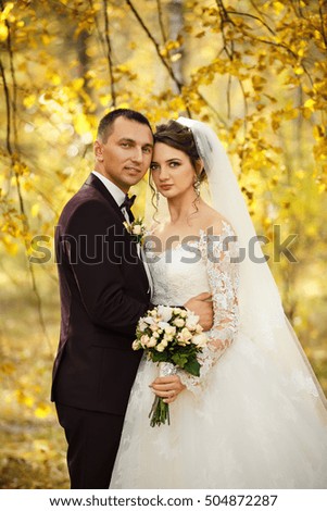 Wedding portrait. Beautiful bride and elegant groom looking at the camera in the autumn yellow forest at their wedding day