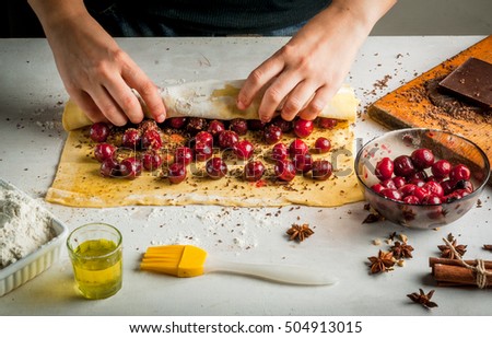 Girl is cooking strudel with chocolate and cherries, wrap it. Hands in the picture