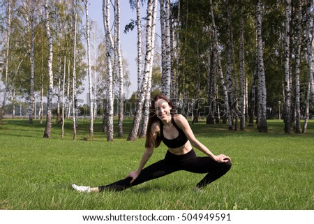 Young sporty teenage model stretching and doing gymnastics and yoga exercises in the open air, wearing black sports wear