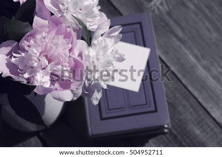 Bouquet of pink peonies on an book an empty white card for the text on a wooden surface. 