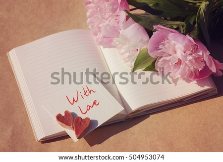 With love. Two hearts on the white card for an inscription "With love" and a bouquet of a pink peonies on an open notebook