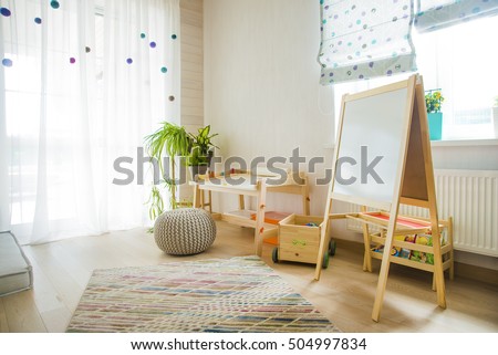 children's room and furniture and natural green flowers on white windowsill. Kindergarten room with easel chair and table for painting. 