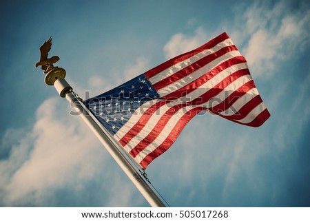 American flag on pole waving in the wind against blue sky and white clouds background. Vintage filter effects.