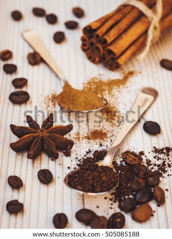 Spoonfuls of ground coffee and cinnamon, cinnamon sticks, coffee beans and star anise on the wooden background
