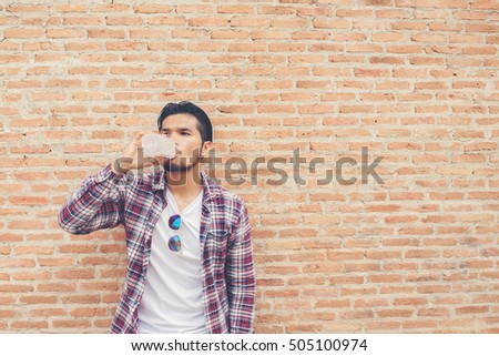 Young hipster bearded man with water bottle in plaid shirt in front of urban background.