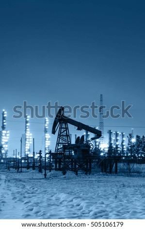 Oil pump and wellhead at the background of refinery by night. Oilfield during winter. Oil and gas industry. Toned.
