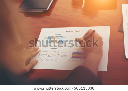 Woman's hand with a pen writing on the business paper. Report chart,busy at work.