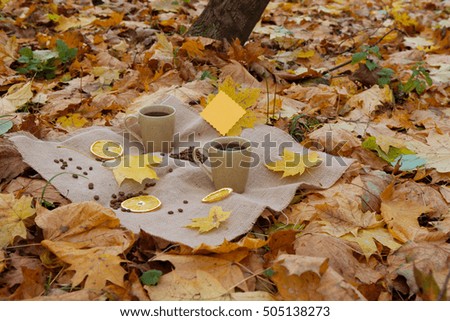 Autumn concept. Two mugs with hot coffee outdoor on autumnal fallen yellow leaves. Heart from coffee beans with empty postcard and dried oranges, autumn still life
