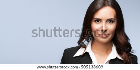 Portrait of happy smiling beautiful young businesswoman, on grey background. Brunette model in black suit - business success concept. Copyspace empty area for some text message or advertise slogan.