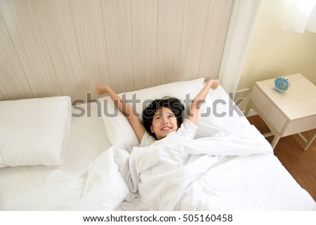 Portrait of happy young Asian girl lying in bed after waking up and stretching arms on the bed after good night sleep. Cheerful kid model with dreamy expression relaxing in the morning. Royalty-Free Stock Photo #505160458