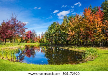 Charming oval pond in the picturesque park. Shining day in French Canada. Concept of recreational tourism. Autumn foliage reflected in clear water of the pond