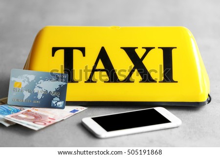 Yellow taxi roof sign with phone, credit card and Euro banknotes on gray background, closeup