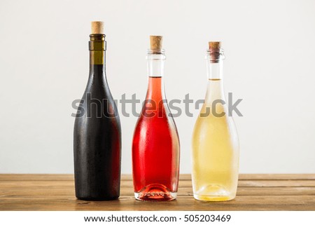 Three different colorful bottles full of wine on wooden table against white background.