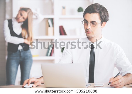 Portrait of serious young businessman using laptop computer in modern office with blurry colleague in the background