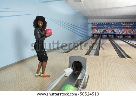 Young woman at bowling alley holding ball, portrait