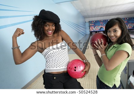 Young women at bowling alley holding balls and posing, portrait