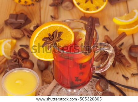 Mulled wine with orange, a jar of honey, nuts and sweets on a background of light wood.