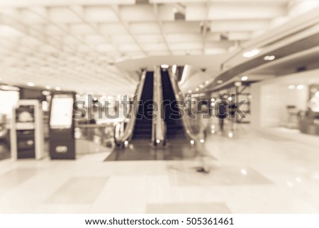 Blur image people in motion in escalators next to information kiosk at modern shopping mall in Asia. Motion blur of shoppers at shopping center. Abstract background shopping mall store interior.