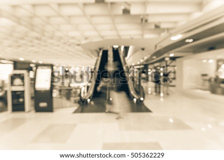 Blur image people in motion in escalators next to information kiosk at modern shopping mall in Asia. Motion blur of shoppers at shopping center. Abstract background shopping mall store interior.