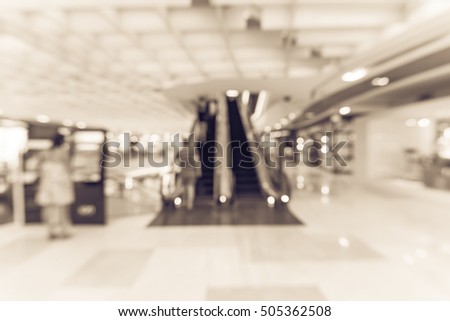Blur image of people looking at the information kiosk next to escalator in modern shopping mall in Asia. Motion blur of shoppers at shopping center. Abstract background of shopping mall store interior
