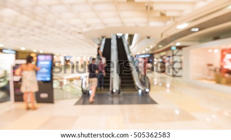 Blur image of people looking at the information kiosk next to escalator in modern shopping mall in Asia. Motion blur of shoppers at shopping center. Abstract background of shopping mall store interior
