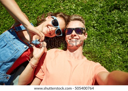 love and people concept - happy teenage couple in sunglasses lying on grass and taking selfie at summer