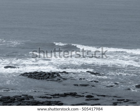 Sea waves on the rocky seashore in blue / gray / black and white shade as an abstract background