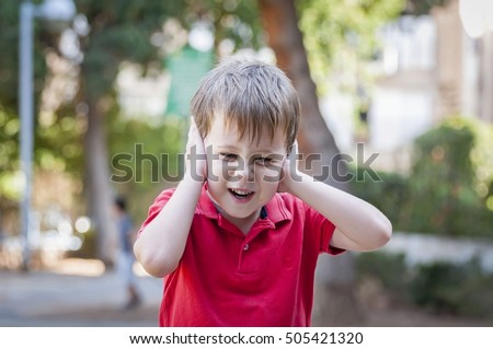 Stressed out little 5-year old Caucasian little boy outside closing his ears and screaming of pain, trauma, traumatic experience and loud noise stock image. Autism, autistic child, asperger syndrome Royalty-Free Stock Photo #505421320