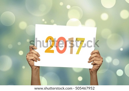 Hand holding 2017 card with abstract light background. Selective focus.