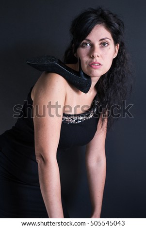 portrait of a dark haired model in black dress on one shoulder and a shoe with a heel