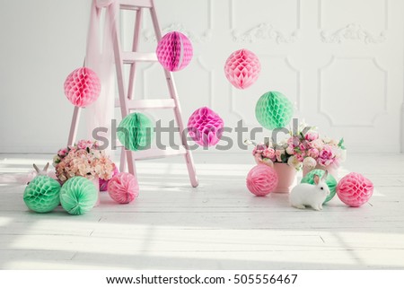 The original bright decor for birthday girl.Pink and green decorative paper balls. White Room decorated with flowers and paper decorations for party.Small white rabbit