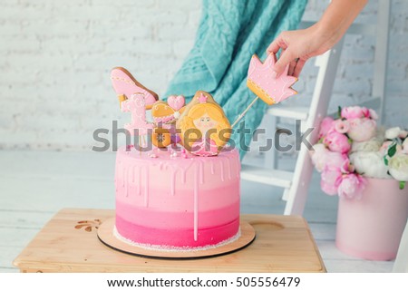 The original pink cake for birthday girl. Pink and yellow gingerbread like a crown, shoe, princess. White Room decorated with flowers for party. Birthday one year old baby girl
