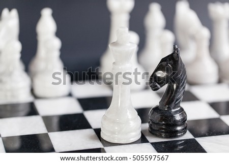 Black chess knight facing a white chess king and the entire army of white chess pieces on a marble chessboard